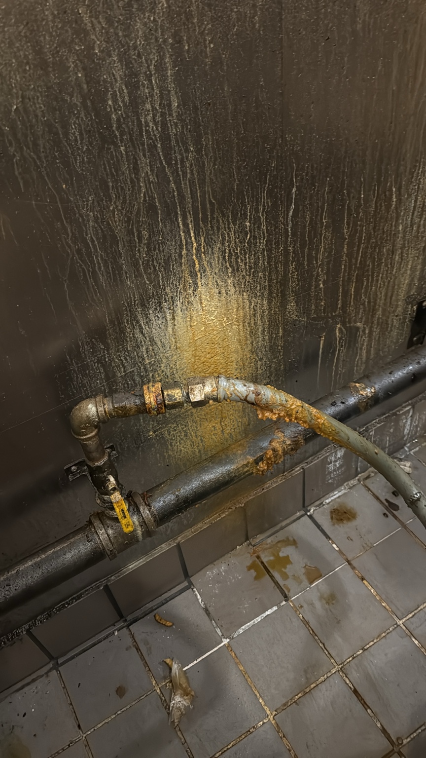 Heavy grease buildup behind commercial kitchen equipment before cleaning
